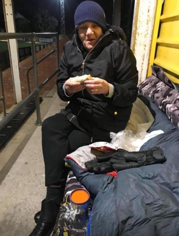 Image of woman outside sitting on a sleeping bag eating a sandwich.
